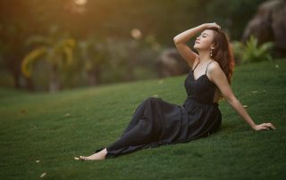 Woman in a black dress posing gracefully on a green lawn at sunset, surrounded by trees and soft golden light