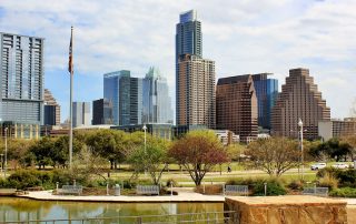 Austin downtown skyline view with modern high-rises, trees, and a reflection pond on a sunny day