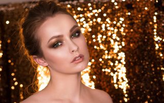 Elegant young woman with green eyes and soft makeup posing against a golden bokeh backdrop, expressing calm confidence through direct eye contact.